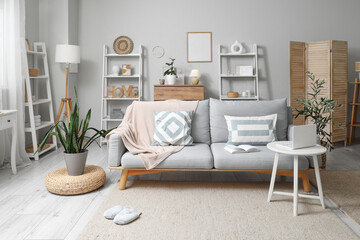 Interior of living room with stylish sofa, shelving units and laptop on coffee table