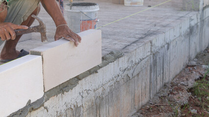 Building a house wall Masonry with lightweight bricks, a male worker is using a hammer to tap the bricks so that they stick to the cement and at the line where the tendons are stretched.