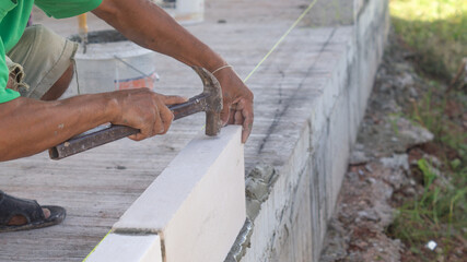 Construction of walls Masonry with lightweight bricks Workers are working, using hammer to knock bricks into place and level.