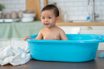 Asian baby taking a bath in a blue tub at home.