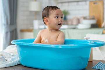 Asian baby taking a bath in a blue tub at home.