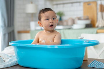 Asian baby taking a bath in a blue tub at home.