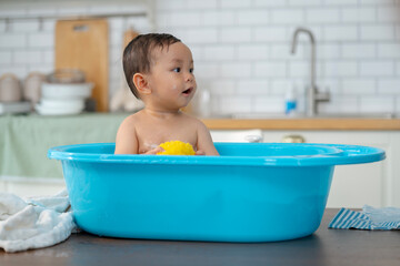 Asian baby taking a bath in a blue tub at home.