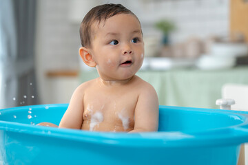 Asian baby taking a bath in a blue tub at home.