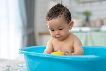 Asian baby taking a bath in a blue tub at home.