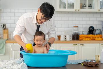Asian baby taking a bath in a blue tub at home.