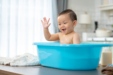 Asian baby taking a bath in a blue tub at home.