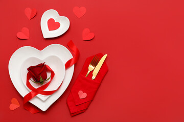 Table setting for Valentine's Day with heart-shaped plates and red ribbon on red background