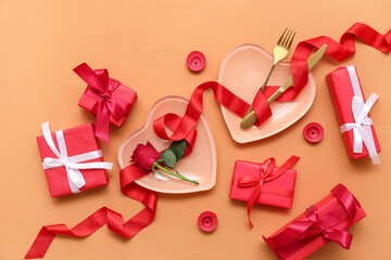 Table setting for Valentine's Day with heart-shaped plates, gift boxes and red ribbon on beige background