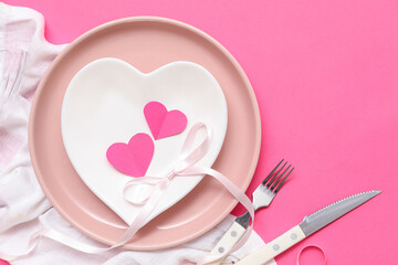 Table setting for Valentine's Day with napkin, ribbon and paper hearts on pink background