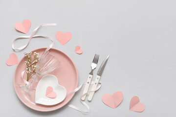 Table setting for Valentine's Day with ribbon, flowers and paper hearts on light background
