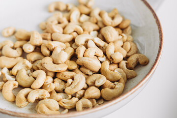 Cashew nuts are poured into white plate on table, close up still life.