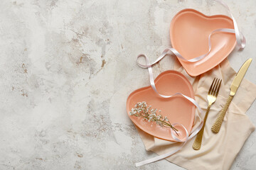 Table setting for Valentine's Day with heart-shaped plates, flowers and ribbon on light grunge...