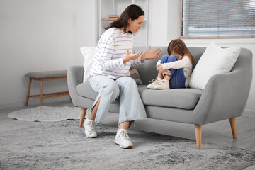 Scared little girl with her quarreling mother sitting on sofa at home. Domestic violence concept