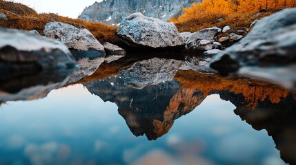 Fototapeta premium A serene landscape showcasing a clear reflection of mountains in water, surrounded by autumn foliage and rocky terrain.