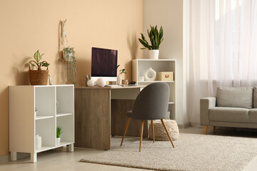 Modern workplace with computer and houseplants near beige wall in room