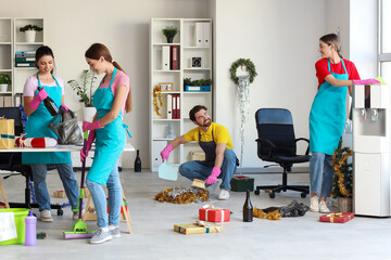 Team of young janitors cleaning in office after New Year party