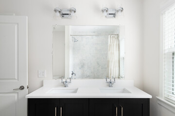 A bathroom with a black vanity cabinet, white countertop, polished chrome light fixtures and faucets, and a marble subway tile shower.
