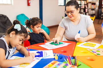 Latina primary school teacher guiding two girls in her class as they paint with colors
