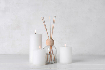 Burning candles and reed diffuser on white wooden table