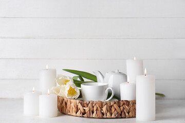 Burning candles with teapot, cup of tea and beautiful tulip flowers on white table