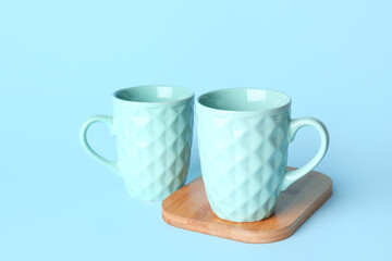 Blue ceramic cups with wooden board on color background