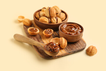 Wooden board and bowl of sweet walnut shaped cookies with boiled condensed milk on yellow background