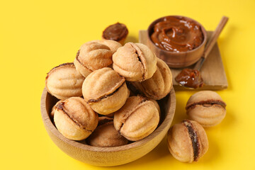 Wooden bowl with sweet walnut shaped cookies with boiled condensed milk on yellow background