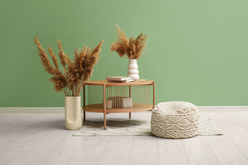 White knitted pouf, coffee table and pampas grass in vases near green wall in room