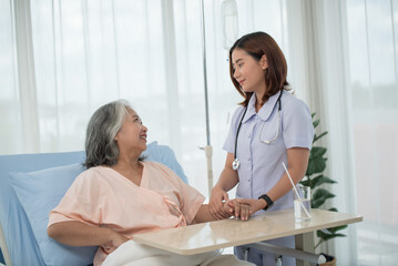 Obraz premium Asian female home nursing holding hand of older lady on the bed and encouraging patient