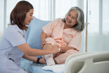 Fototapeta premium Asian female nurse bandaging foot of elderly woman patient