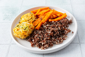 A delicious and wholesome plate featuring brown rice, sweet potatoes, and chickpea pancakes made with squash, perfect for a balanced and nutritious meal, fresh salad of tomatoes and cucumbers