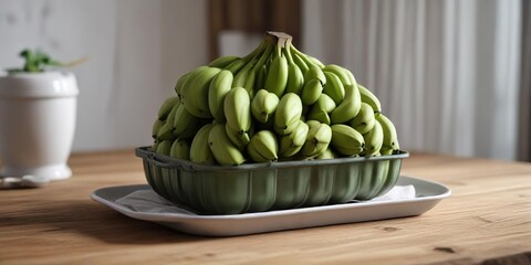 A bunch of green bananas piled high in a shallow metal container positioned next to a simple white ceramic plate placed on a worn wooden dining table top, rustic, plate, container