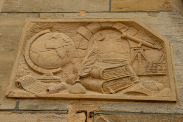 sculpture en pierre en bas relief avec un globe terrestre un vieux livre et une lunette astronomique