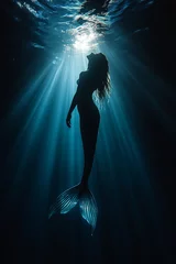 Silhouette of a mermaid swimming in deep blue water with sunlight filtering through