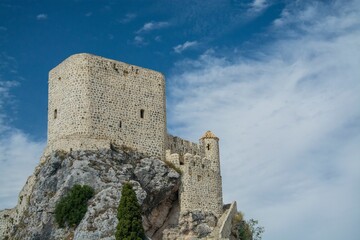 Medieval stone castle on a rocky hilltop under a vibrant blue sky in Spain