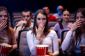 Three friends are watching a movie in cinema and they are eating popcorn.
