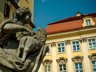 Detailed stone statue of a figure holding a sheep in front of a historic building in Poland