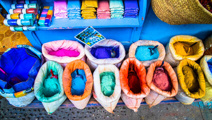 Bags filled with vibrant colored pigments (blue, red, yellow) displayed at an artisanal market in Chefchaouen, Morocco, evoke art and local culture.