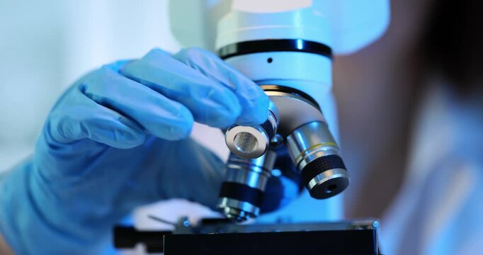 Scientist chemist microbiologist turns lenses of microscope and uses different magnifications in laboratory