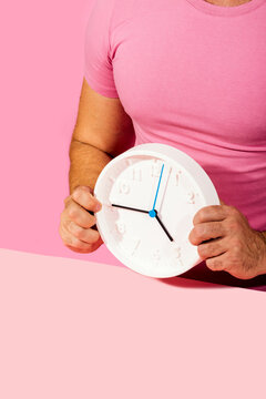Man Holding White Clock Against Pink Background with Time Concept