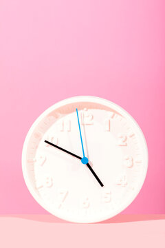 Minimalist white clock against pastel pink background