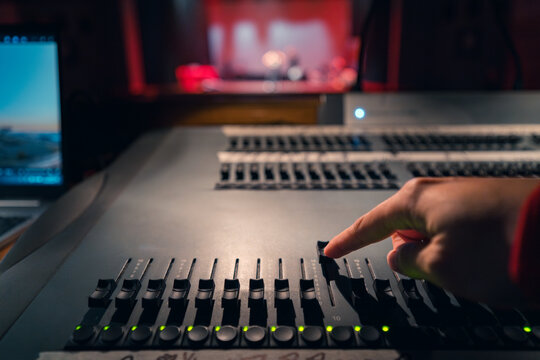 Hand adjusting soundboard controls in dimly lit studio