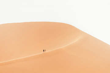 Two far away figures of a couple walking up a sand dune in the desert