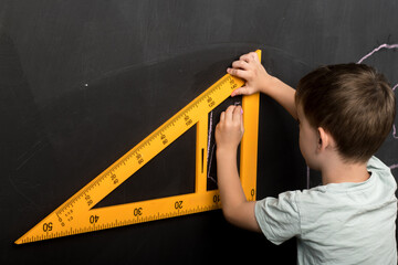 A young student uses a large yellow protractor to draw precise lines on a blackboard, emphasizing...