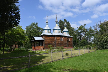A charming wooden church with blue domes and crosses, surrounded by lush greenery and a rustic...