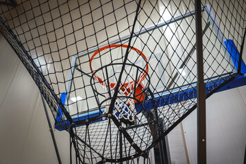 A basketball hoop with a netted return system is mounted on a glass backboard in a modern indoor...