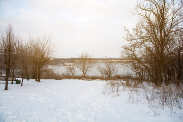 Winter landscape with snow-covered ground, bare trees, and a distant dam over a river. A serene and tranquil scene perfect for nature and winter-themed projects