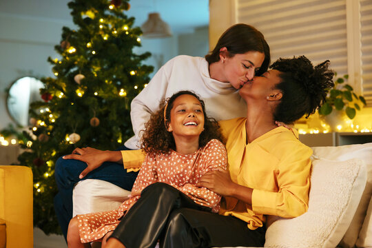 Loving women kissing on sofa near daughter