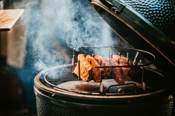 smoky barbecue grilling ribs in open bbq with wooden handles.